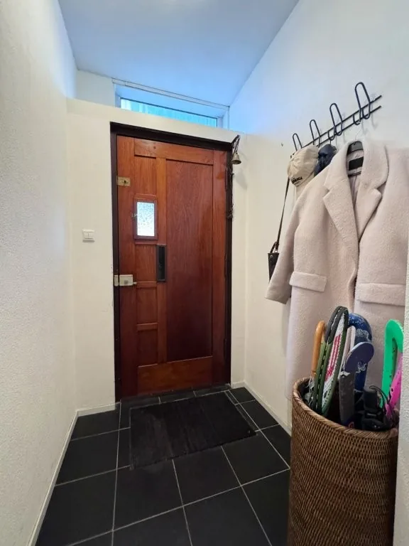 Entree met houten voordeur, tegelvloer en garderobe